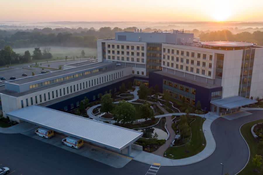 Regional hospital campus at dawn with rooftop helipad, ambulance canopy and a healing-garden courtyard.